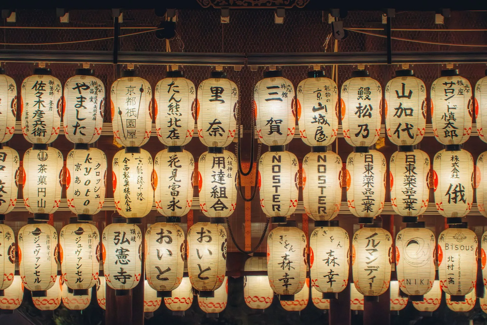 Rows of glowing paper lanterns with painted kanji at a shrine
