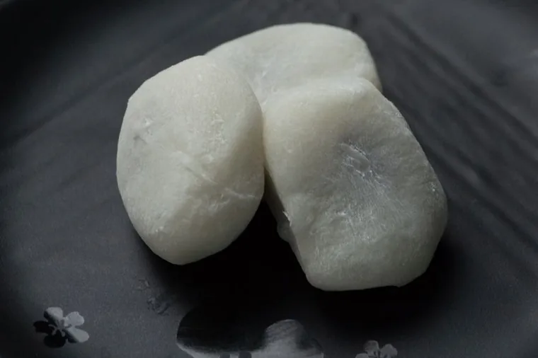 Two plain white rounds of mochi on a dark plate